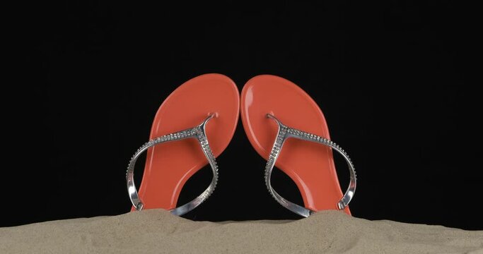 Pair of pink flip flops embellished with rhinestones stick out of the sand. Panorama. Isolated