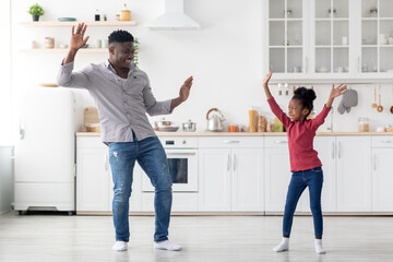 Funny african american father and daughter damcing at kitchen
