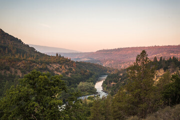 A river flows through forested hills at sunset