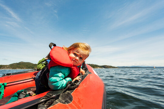 A young child sits on front of rubber boat looking at camera