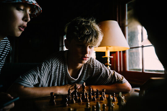 Boys Play Chess together in a rustic cabin by window light