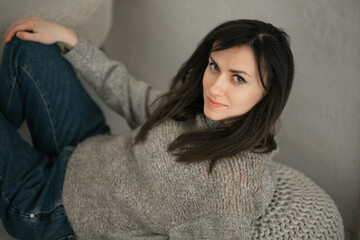  Portrait of a young Ukrainian girl sitting on a footstool on the floor

Young Ukrainian brunette sitting on a ottoman woman in jeans and a sweater has long hair brown eyes portrait in the interior