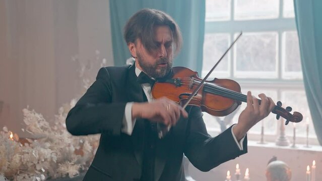 A Young Girl And Man Plays The Violin In A Beautiful Retro Room With Flowers And A Piano.