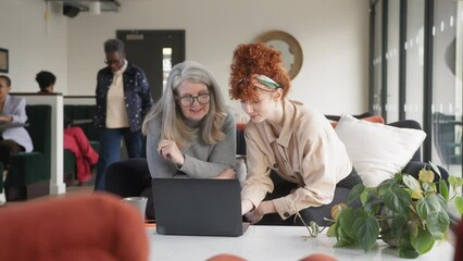 Slow motion of senior and young white business colleagues discussing and smiling with laptop in open plan office space