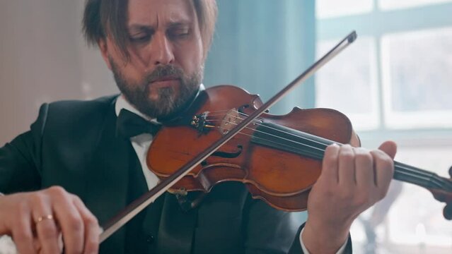 A Young Girl And Man Plays The Violin In A Beautiful Retro Room With Flowers And A Piano.