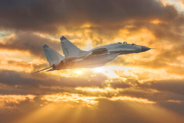 Military Aircraft flies in the sky lit by the setting sun and rays.