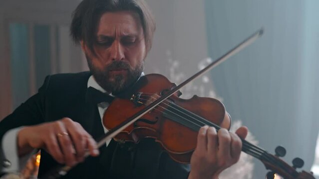 A Young Girl And Man Plays The Violin In A Beautiful Retro Room With Flowers And A Piano.
