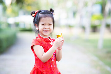 Portrait cute Asian girl holding Chinese golden. Sweet smiling children are happy. Child celebrate Chinese New Year. Kid was wearing beautiful red qipao Cheongsam. Female aged 5 years old.