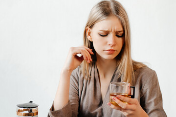 Good-looking girl is suspiciously looking at the glass of tea she is holding. Young woman received a wrong taste of tea. Concept of cafe