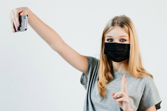 Cute Girl Is Taking A Selfie In A Black Mask And Showing A Peace Sign. Young Woman Is Wearing A Mask In All Public Places And Encouraging People To Do The Same. Concept Of Health