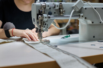Seamstress is sewing beige fabric in a sewing workshop. The process of sewing fabric. The needle of the sewing machine is in motion.