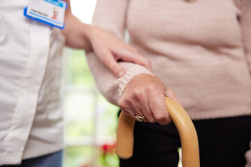 Close Up Of Senior Woman With Hands On Walking Stick Being Helped By Care Worker