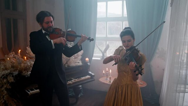A Young Girl And Man Plays The Violin In A Beautiful Retro Room With Flowers And A Piano.