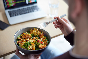 Close Of Man Eating Healthy Vegan Lunch At Office Deak Whilst Using Laptop