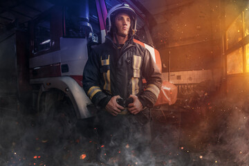 Fototapeta na wymiar Proud firefighter posing around fire truck indoors fire station