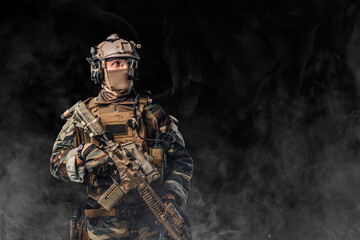 Equipped soldier holding rifle against black background with fog
