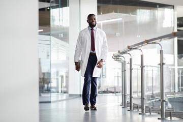 Cheerful young black scientist walking by laboratory and smiling - Powered by Adobe