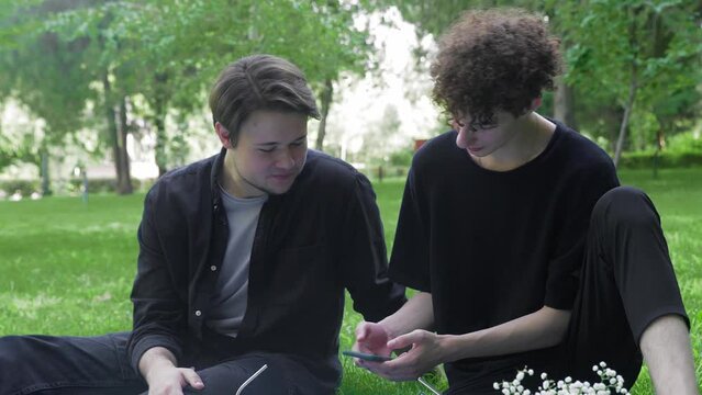 Two young guys looking at the phone in nature in the summer. LGBT