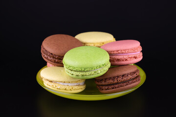 Colored cakes macaroons group in green saucer on black background. Cooking concept delicious sweet food.