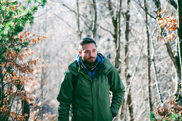 Attractive Caucasian male hiking in forest. Young hiker walking uphill through the mountain woods in late winter.