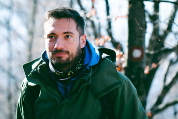 Attractive Caucasian male hiking in forest. Head shot of young hiker posing in front of trail path mark.