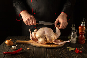 The cook cuts raw broiler chicken with a knife. Cooking a national dish in the restaurant kitchen with chicken