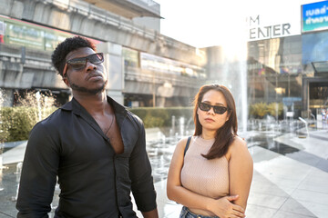 Portrait of two multiracial serious friends with sunglasses stanging on a mall