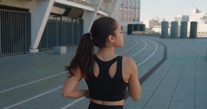 Rear back view of happy athletic woman jogging outdoors in slow motion. Fitness girl doing cardio workout, running in the morning on city streets