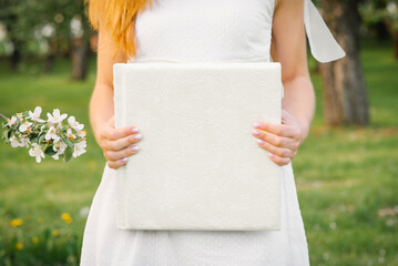 A white-covered wedding photo album is held by a woman in a white dress