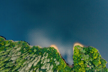 Top view of the green forest on the river bank with dark blue water and reflected sky