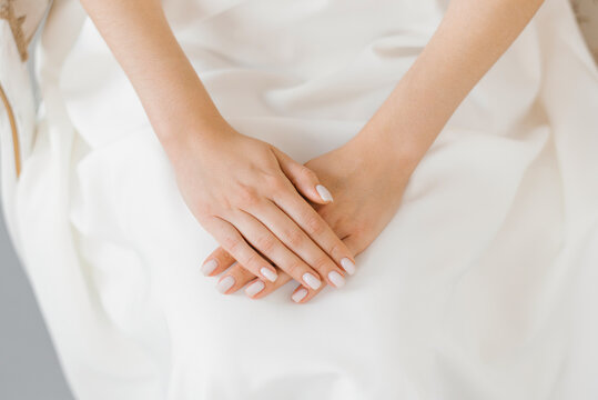 Delicate manicure of the bride, the hands of a young woman lie on a white wedding dress