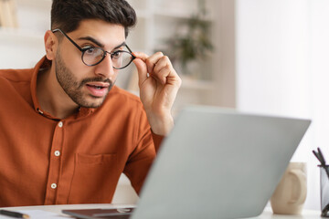 Shocked Arab guy using laptop looking at screen