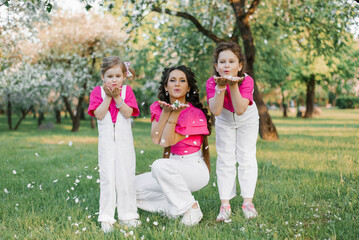 Obraz premium Cute mom and two daughters blowing on the fallen petals of apple blossoms in the spring garden. Outdoor activity. Sweet moments family