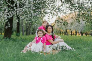 Naklejka premium Cute mom and two daughters are having a picnic in the spring garden. Outdoor activity. Sweet moments family