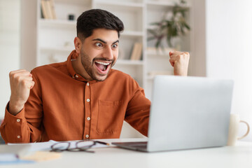 Arabic man using laptop celebrating success shaking fists screaming yes
