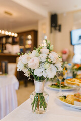 A delicate bridal bouquet of the bride stands in a glass vase on a festive banquet table