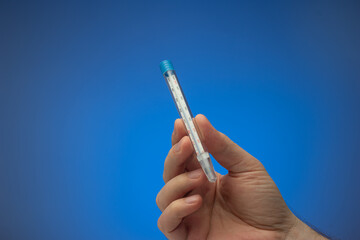 Mercury glass thermometer held in hand by Caucasian male. Close up studio shot, isolated on blue...