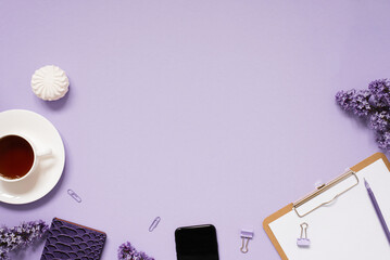 notepad and pen, paper clips and clips with a layout of the place to copy. Home office desktop with top view, decorated with lilac flowers, a cup of tea