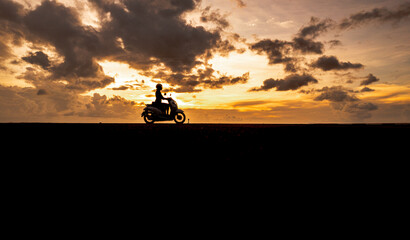 Silhouette riding a scooter on the seashore during sunset