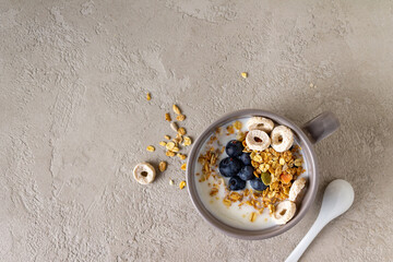 yogurt, granola, blueberries in a cup on gray plaster, copy space