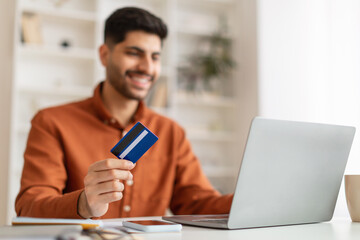 Smiling young man using pc and credit card, selective focus
