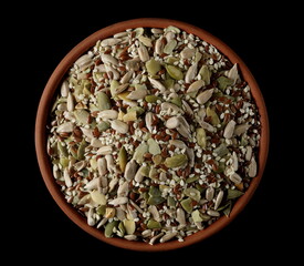Mix seeds, sunflower, sesame, linseed and pumpkin seed in clay pot isolated on black, top view