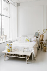 Light airy white with yellow shades bedroom in the house. A cozy bed and vases with spring branches. Natural room decor