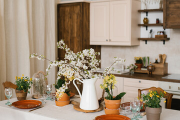 Fototapeta na wymiar A bouquet of spring white flowers on branches in a vase on the kitchen table. Scandinavian style of the interior and decor of the house