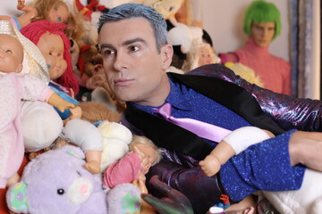 Fashionable eccentric man with many dolls and toys in bed