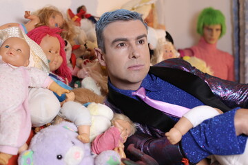 Fashionable eccentric man with many dolls and toys in bed