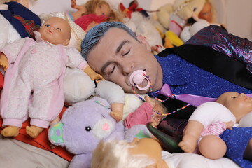 Funny adult man with eccentric outfit sleeping with many toys and sucking pacifier