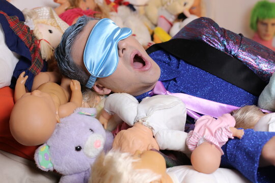 Eccentric Man Surrounded By Weird Dolls Snoring 