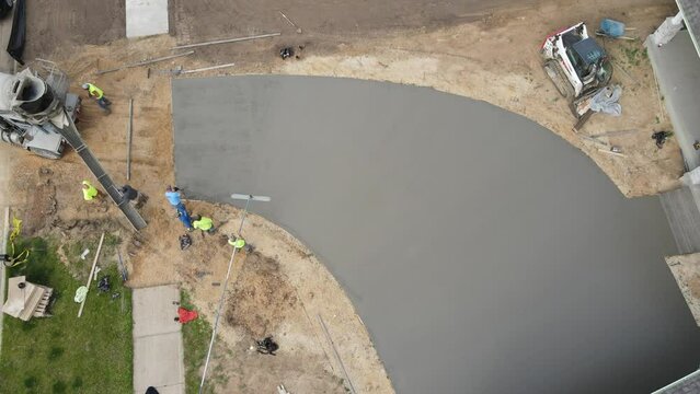 Birds eye view of concrete crew putting the finishing touches on a new driveway in fast pace. Teamwork to finish up the job. Floating the concrete. Dirt all around the edges of new construction. 