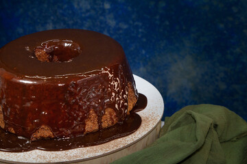 Detail of homemade chocolate cake with syrup poured on top. Dark mottled blue background in the background.